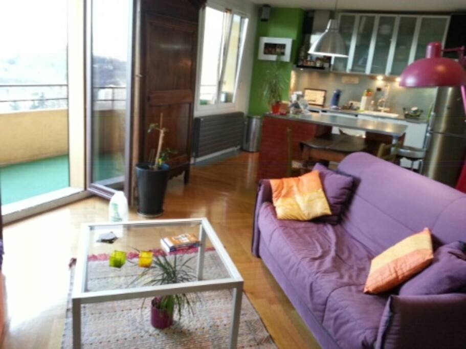 Pièce à vivre avec salon et cuisine intégrée donnant sur balcon.