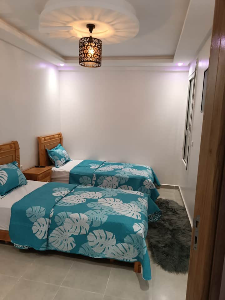 Спална соба со два единечни кревета, ноќно шкафче, прозорец за природна светлина, како и 32-инчен паметен телевизор со IPTV и Netflix за забава.