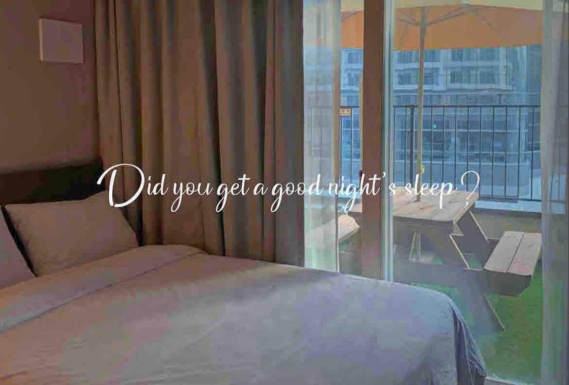 A comfortable sleeping area is presented, featuring a spacious bed with soft bedding. Sheer curtains allow natural light to filter in, illuminating the space. A balcony is visible, showcasing outdoor seating surrounded by greenery.