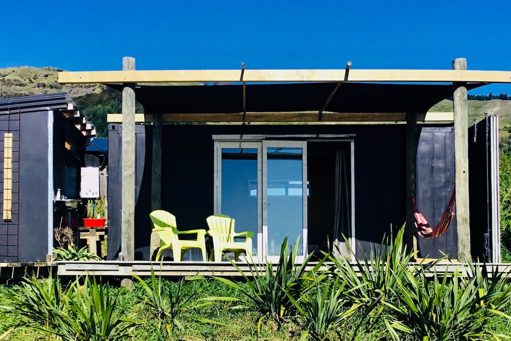 The front of the shipping container cabin, bifolding doors, deck, hammock, bathroom to the left.