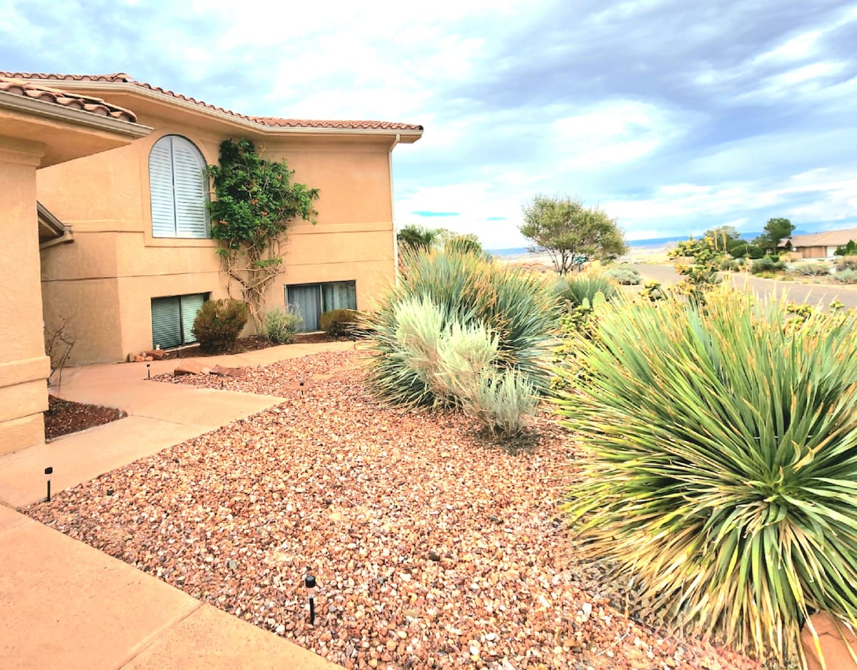 A well-maintained outdoor area surrounds the private suite, featuring a landscaped garden with various desert plants and decorative rocks. The structure has large windows, allowing natural light to enter, and the scenery beyond includes distant views of the landscape.