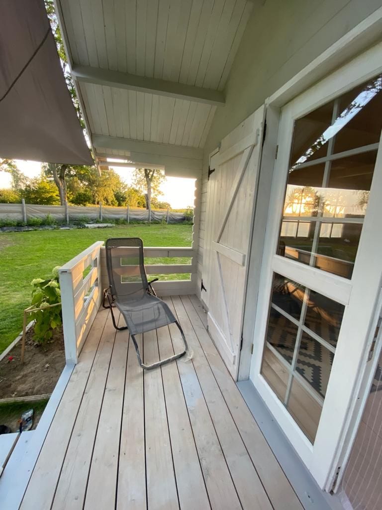 A wooden deck area features a single reclining chair, positioned near glass doors leading into the interior. Soft light from the setting sun enhances the greenery visible beyond the railing, creating a calm outdoor space for relaxation.