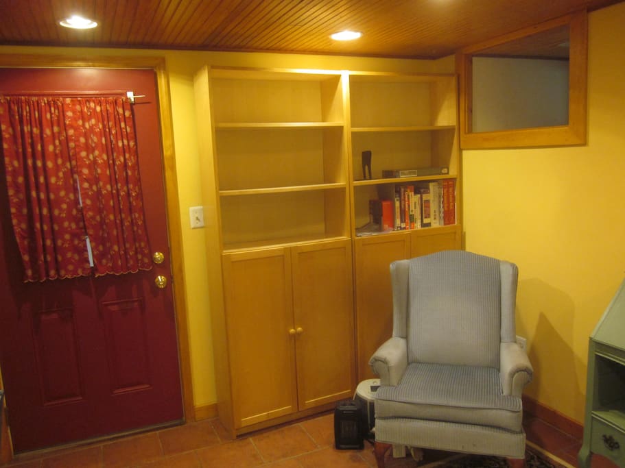 Upholstered reading chair beside desk, library shelving and storage cabinets. Door leads to laundry, foyer, and exit door.
