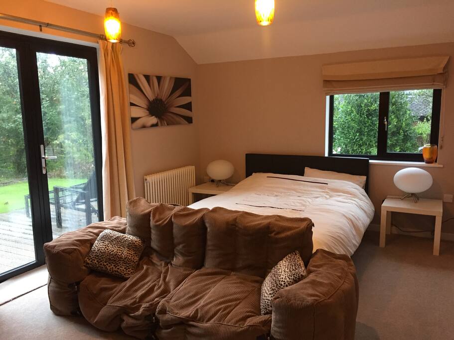 Main room with kingsize bed and beanbag sofa, patio doors lead onto decking and garden