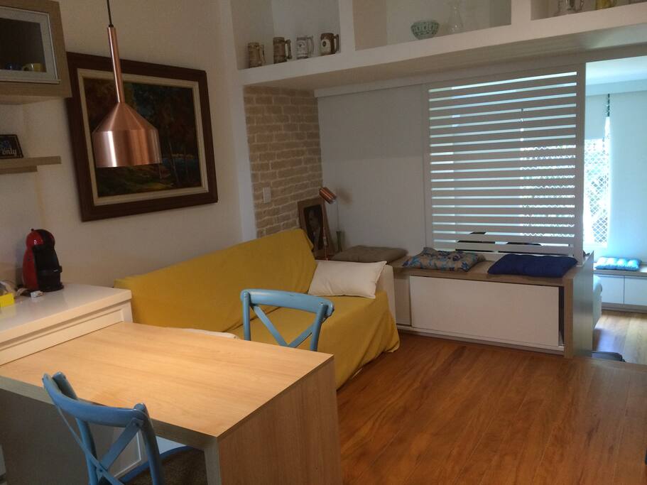 Sala com sofá cama e tv, com uma divisória com o quarto.