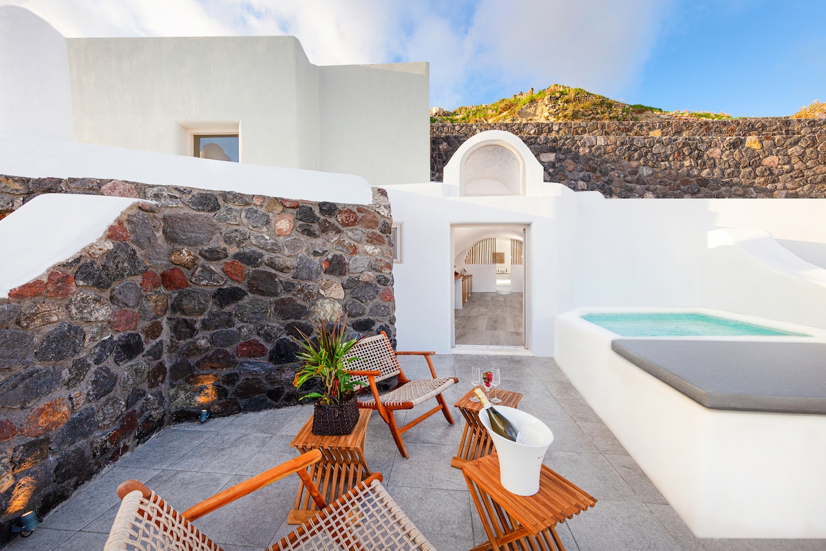 An outdoor area is presented with modern lounge chairs surrounding a small pool. The stone walls provide a natural backdrop, while the bright sky adds a sense of openness. A minimalist design is complemented by a few potted plants and a small table.