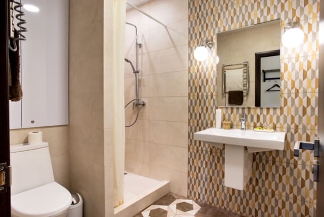 The bathroom features a modern design with a walk-in shower and sleek, tiled walls. A spacious sink is complemented by a large mirror above. Soft lighting is provided by round fixtures, while decorative tiles add a unique touch to the floor.
