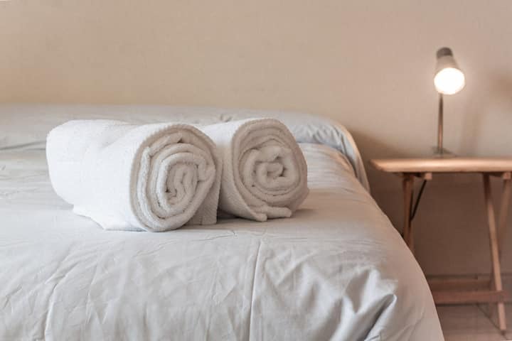 ห้องหลักที่มีระเบียงและวิวขอบฟ้าของ CDMX พร้อมเตียงคู่โต๊ะอ่านหนังสือและโคมไฟข้างตู้เสื้อผ้าพร้อมลิ้นชักและตะขอพื้นที่ทำงานพร้อมโต๊ะเก้าอี้และโคมไฟตั้งโต๊ะ ผ้าห่มผ้าฝ้ายผ้าเช็ดตัว