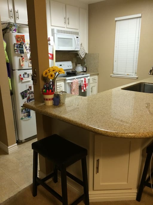 Kitchen with oven, dishwasher, microwave, dishes and utensils, and 2 stools