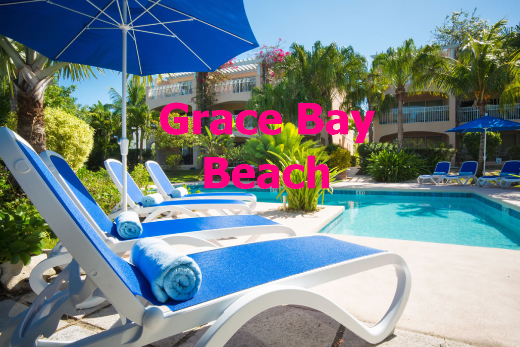 A serene pool area is surrounded by lush greenery and palm trees. Blue sun loungers with rolled towels are positioned alongside the inviting turquoise water of the private pool, under large blue umbrellas. The setting offers a relaxing outdoor space for guests.