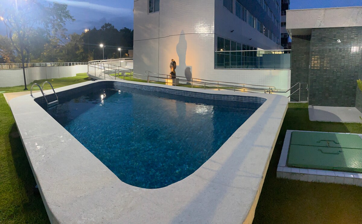 An outdoor swimming pool is surrounded by a well-maintained grassy area. The pool features a smooth, textured rim and is equipped with a small set of stairs leading into the water. Night lighting casts a gentle glow on the water's surface.