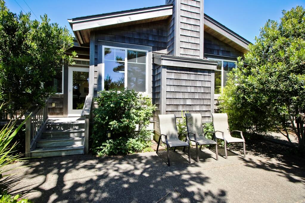 Front view of Valentines House. Landscaped yard with a stone patio, chairs and gas BBQ.