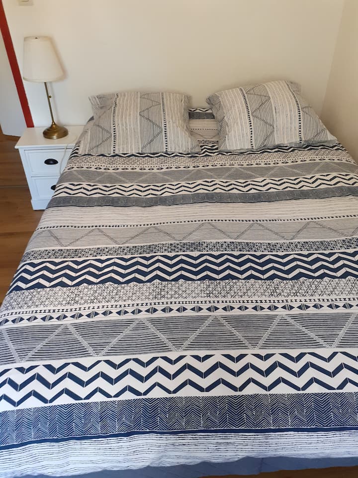 Пространа спална соба, опремена со двоен кревет со постелнина, гардероба со полици, гардероба и ноќна масичка.