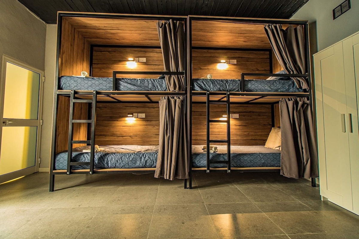 Bunk beds are arranged in a compact layout, with two sets on display. Each bunk is enclosed with fabric curtains and features a light fixture above. The surrounding area is well-maintained, showcasing tiled flooring and neutral-colored walls.