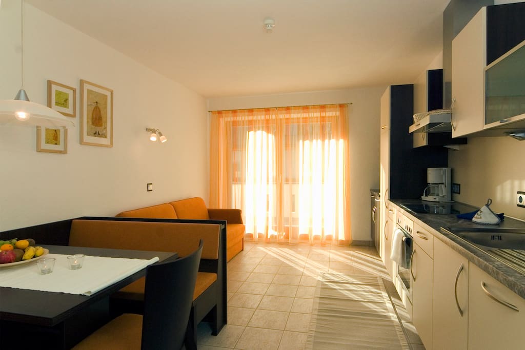 Wohnküche mit der ausziehbaren Couch und Esstisch und breitem Balkon