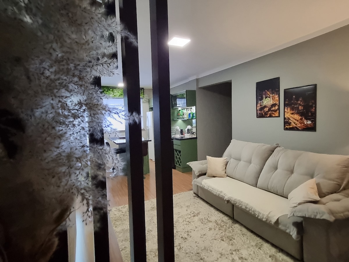 A spacious living area is visible, featuring a comfortable gray sofa in front of a soft area rug. Two framed photographs adorn the wall, adding a touch of character. The kitchen can be glimpsed in the background, showcasing additional modern decor.