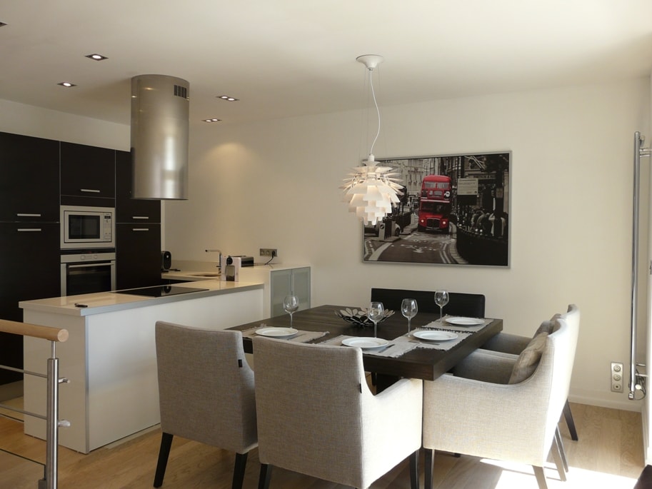 A modern open-plan kitchen and dining area features sleek cabinetry and stainless steel appliances. A dining table is set for four, complemented by soft gray chairs. An artistic black-and-white photograph of a double-decker bus adds a stylish touch to the wall.