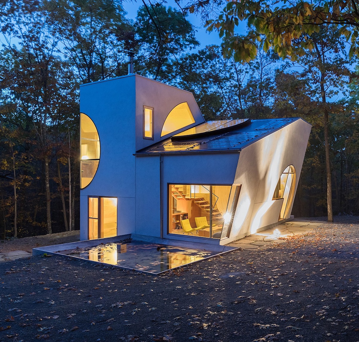 A white, modern home designed by Steven Holl, is captured at dusk and lit warmly from within.