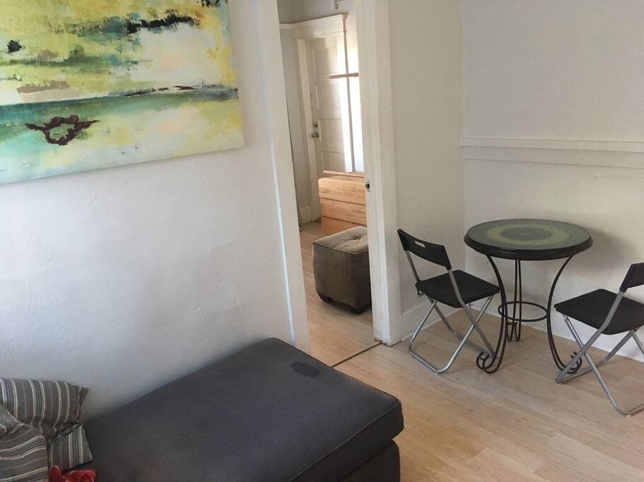 The entry room. Comfy chaise lounge for you to relax on, and a table to enjoy meals at. The door to the left connects to the bedroom.