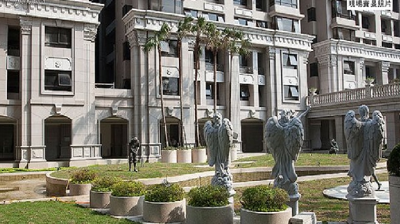 The exterior features a grand building with a classic architectural style. Several ornamental statues are positioned in the well-maintained garden area, surrounded by lush grass and neatly trimmed shrubs, adding elegance to the outdoor setting.