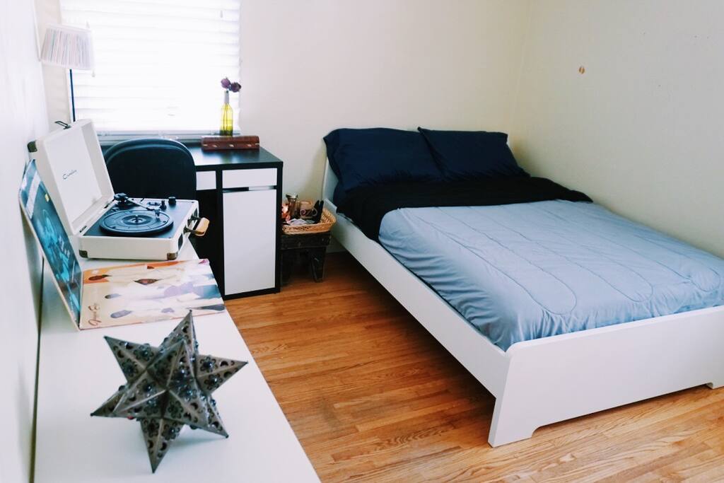 Queen sized bed with desk, and bed-side stool with tea, water, and snacks.