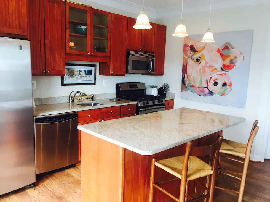 Bright and open kitchen with granite counters, island, stainless steel appliances, microwave and furnished with full set of dishes and cookware.