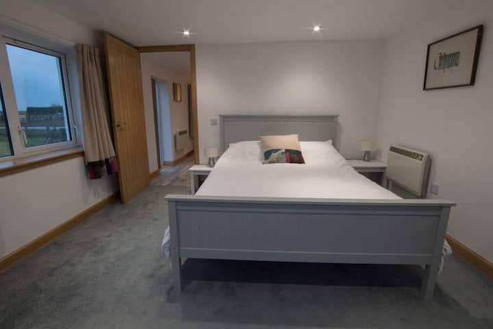 Dormitorio con cama king, televisión inteligente y puertas de patio en la terraza con vistas al mar.