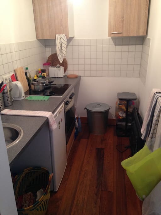 Küche mit Herd und Kühlschrank. Kochutensilien sind vorhanden.