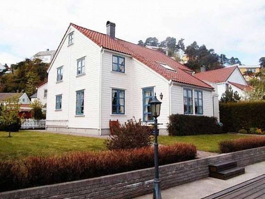 Eldre bilde av eiendommen tatt fra sjøen, med hage og brygge i forgrunnen