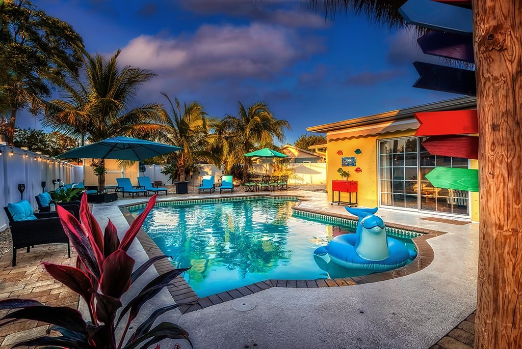 A private pool area is surrounded by palm trees and shaded by umbrellas. The inviting water reflects blue skies, while a colorful float adds a playful touch. Comfortable seating is arranged around the pool, creating a relaxed outdoor atmosphere.