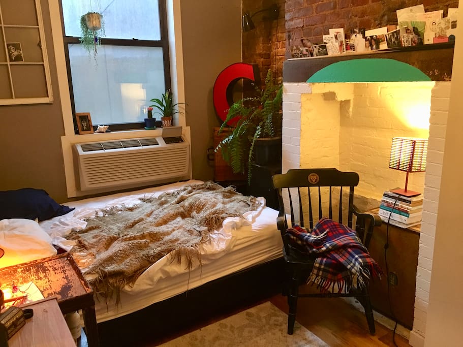 Here you see the bedroom window, the AC/heater, queen bed, the brick fireplace and a nice reading chair.