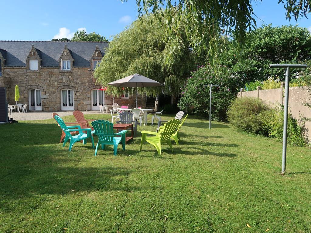 A spacious garden area is displayed, featuring colorful lounge chairs arranged in a casual circle. A large umbrella provides shade over a dining table. Lush greenery surrounds the space, while a clothesline stands to the side, contributing to the serene outdoor environment.