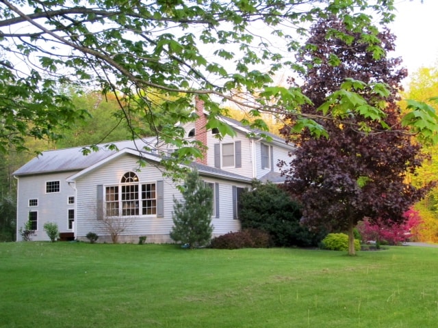 The exterior of the lodge features a two-story design, framed by a lush green lawn. Decorative trees and shrubs accentuate the property, while a large window invites natural light into the interior. A calming atmosphere is created by the surrounding scenery.