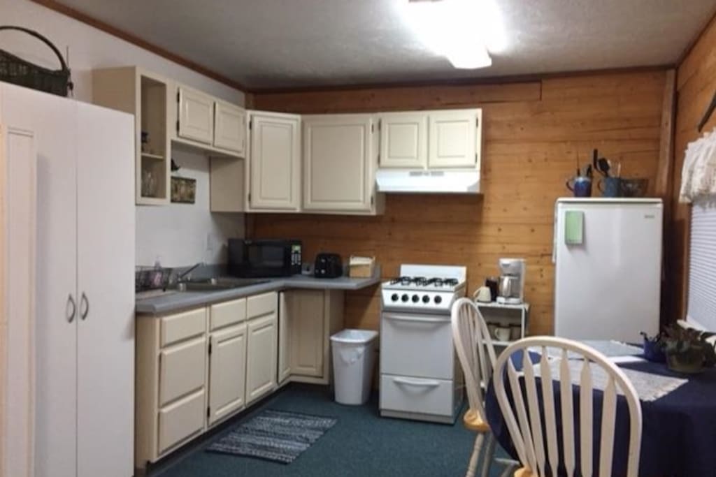 A kitchen featuring a microwave, coffee pot, stove with natural gas burners and refrigerator. Armoire for your clothing.