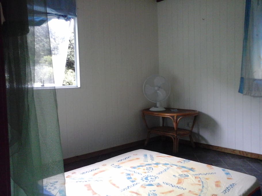 Chambre modestement meublée avec une petite table sur la droite et un meuble de chevet sur la gauche.