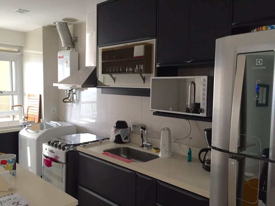 American Kitchen with access to the balcony, stainless Refrigerator, Microwave, cooker, fume cupboard, gas heater, washer, laundry sink, coffee machine, water filter, toaster, glasses, cutlery, dishes, pans and a lot of cabinets.