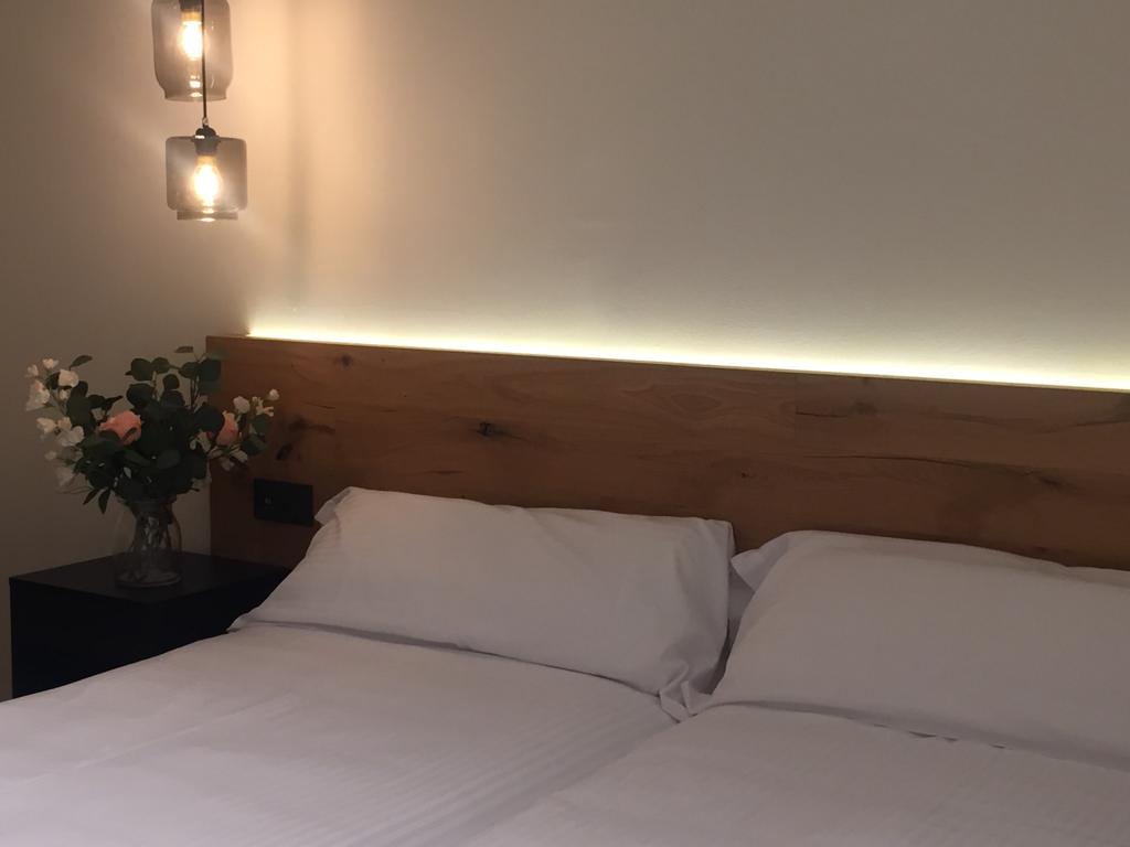 A cozy sleeping area is presented with two spacious beds, configured either together or separately as preferred. Soft white linens are neatly arranged, complemented by a decorative floral arrangement and modern light fixtures above the headboard, providing gentle illumination.
