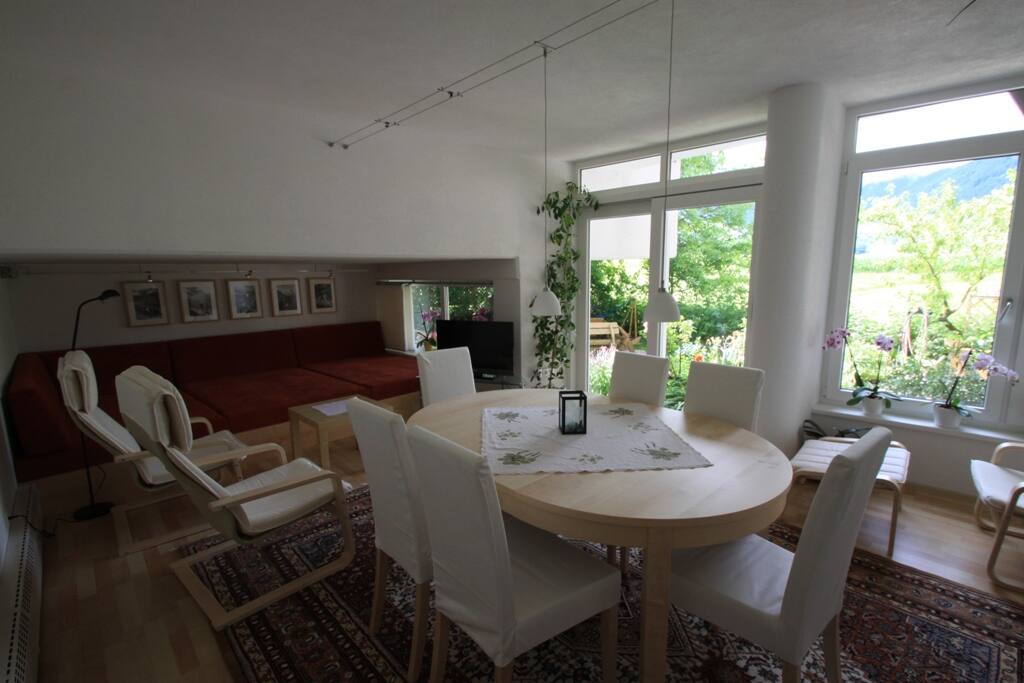 Wintergarten mit großem Tisch, Liegefläche, kleinem Balkon und Aussicht auf den Garten