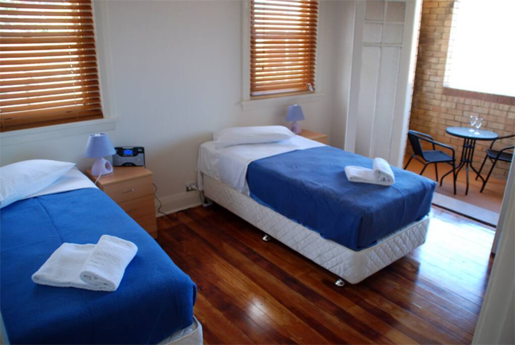 Bedroom with queen and single beds, and wardrobe. Balcony with outdoor setting.