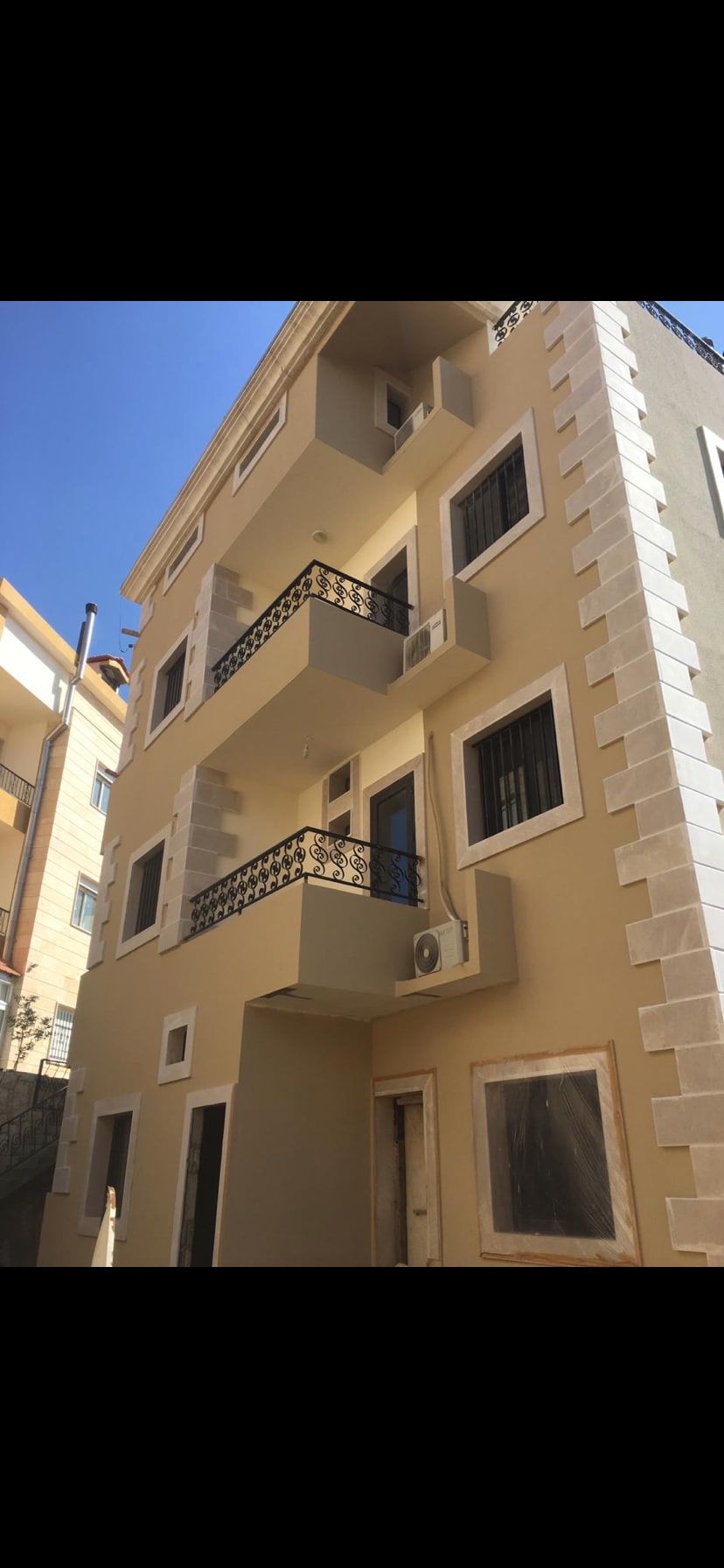 The exterior of the house is shown, featuring a three-story structure with multiple balconies adorned with decorative railings. Clear windows illuminate the light-colored facade, which showcases a blend of modern and traditional architectural elements.