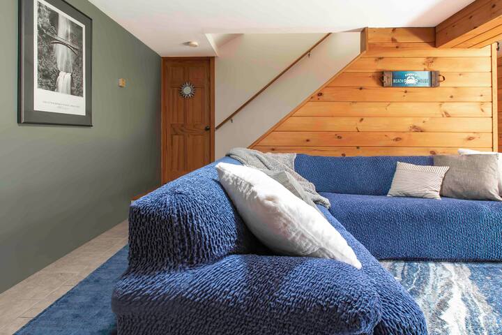 Მისაღები ოთახის ქვედა დონის სივრცე დიდი კუთხის სექციით, სამუშაო მაგიდით, შეზლონგით და 55-დუიმიანი 4K სმარტ-ტელევიზორით 