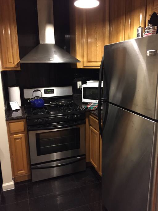 Kitchen with huge fridge, microwave, toaster oven, and gas stove with exhaust hood.
