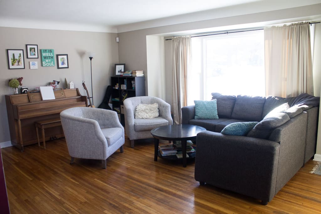 Spacious living room with good natural light, charming fireplace wall, and piano. TV can be placed above fireplace mantle (prior to arrival) if desired.