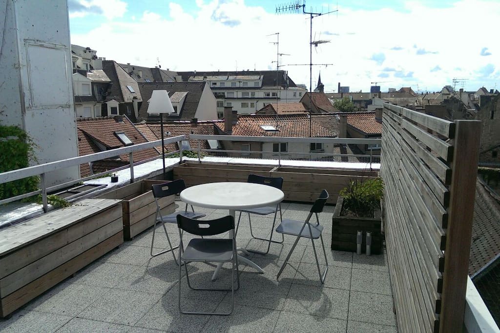 Terrasse d'environ 25m carrés avec une table, chaises, lumière, transats et un parasol pour les beaux jours, vue panoramique sur les toits de Strasbourg et la cathédrale.