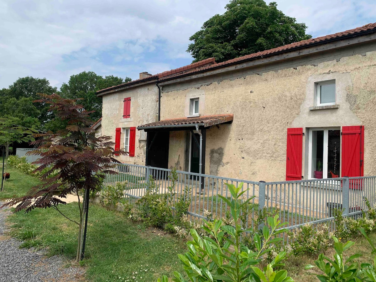 The exterior of the bed and breakfast features a rustic stone facade complemented by bright red shutters. A covered porch provides access to the entrance, while well-maintained greenery surrounds the property, enhancing the inviting atmosphere.