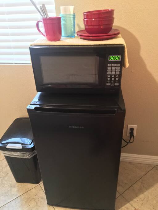 Personal kitchenette that includes a microwave, mini fridge/freezer, dinnerware and silverware.