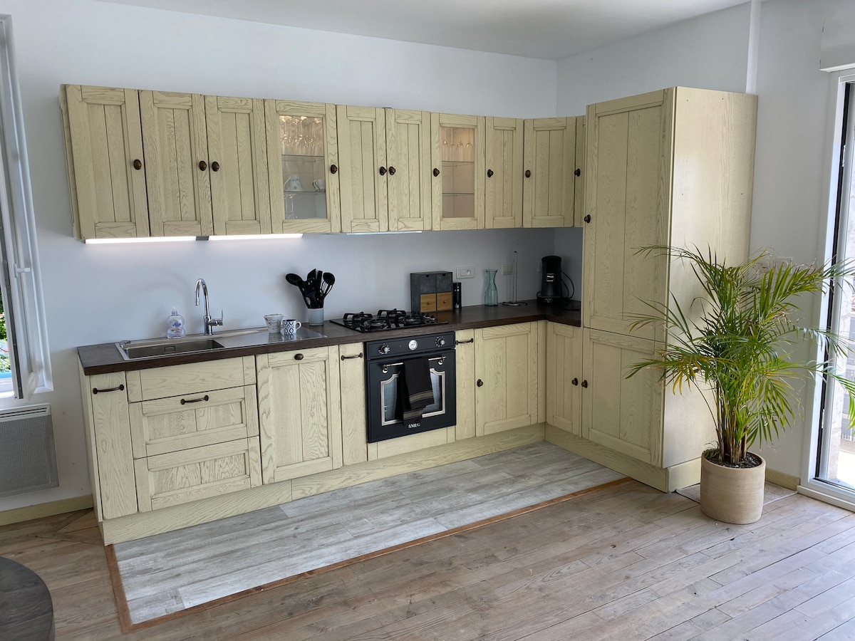 A well-equipped kitchen features light-colored cabinetry with glass-fronted upper cabinets. A gas stove is centered with a black oven below, complemented by a sleek counter space. A potted plant adds a touch of greenery, and natural light filters through the nearby window.