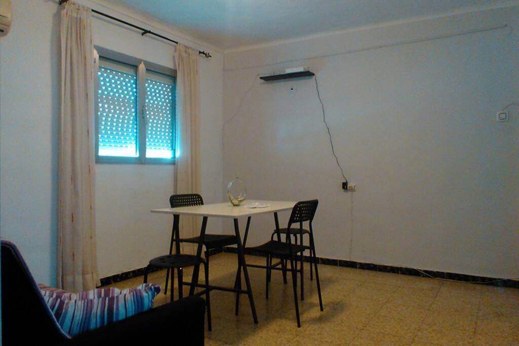 Sitting room with sofa bed, air conditioner, table and chairs.