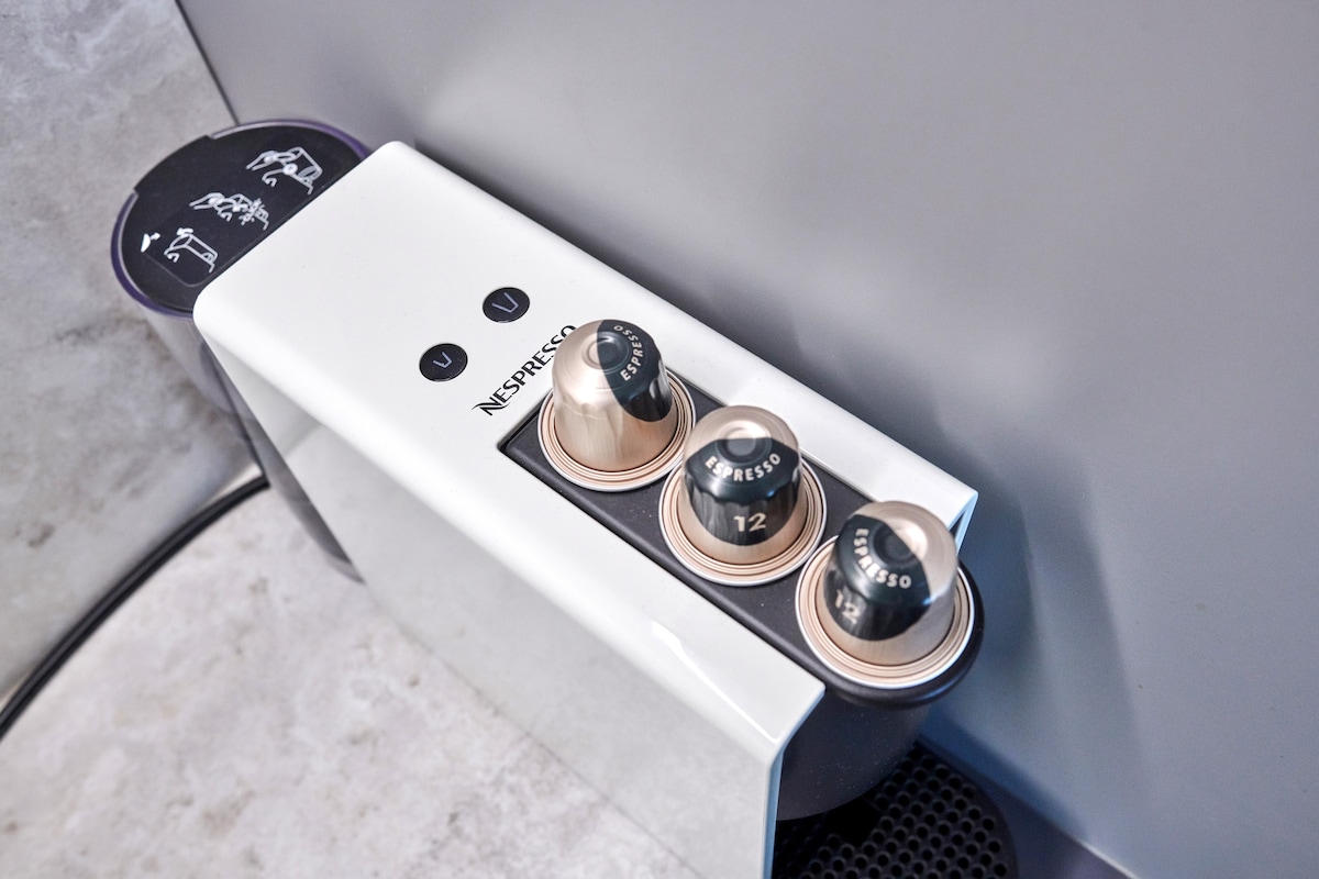 A Nespresso coffee machine displays three different pods, labeled with numbers for various coffee strengths. The machine features a sleek white design with black accents, positioned against a textured surface, providing a modern touch to the kitchen space.