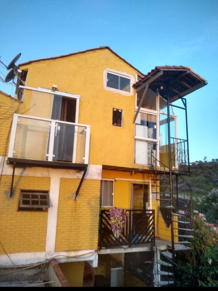 A bright yellow two-story building features multiple balconies with glass railings. A spiral staircase leads to the upper level. Large windows offer natural light, and decorative elements add a touch of character to the exterior.